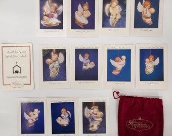 May include: A set of 12 Christmas ornaments featuring angels with babies. Each ornament is packaged in a white card with a blue background and the text "And His Name Shall Be Called..." The ornaments are part of a collection called "Ornament Collection".