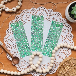 May include: Three rectangular bookmarks with a green, abstract pattern are displayed on a white doily. The bookmarks have a watercolour effect with a white background and green shapes. A small succulent in a white pot is in the background.