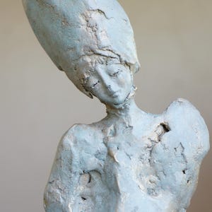 Peut inclure: Une sculpture abstraite bleue d'une personne avec une grosse tête ronde et une surface texturée.
