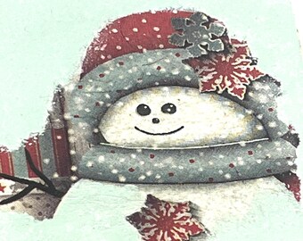 May include: A festive snowman design on a pale blue backdrop. The snowman is adorned with a red polka-dot hat, a grey scarf with white spots, and a red and white striped scarf. A red snowflake and a red star embellish the design. The snowman has a smiling face.