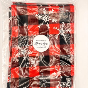 May include: A red and black buffalo plaid fabric with white snowflake designs. The fabric is packaged in a clear plastic bag with a white circle label that reads "Handmade by Doctor Care" and includes a website address.