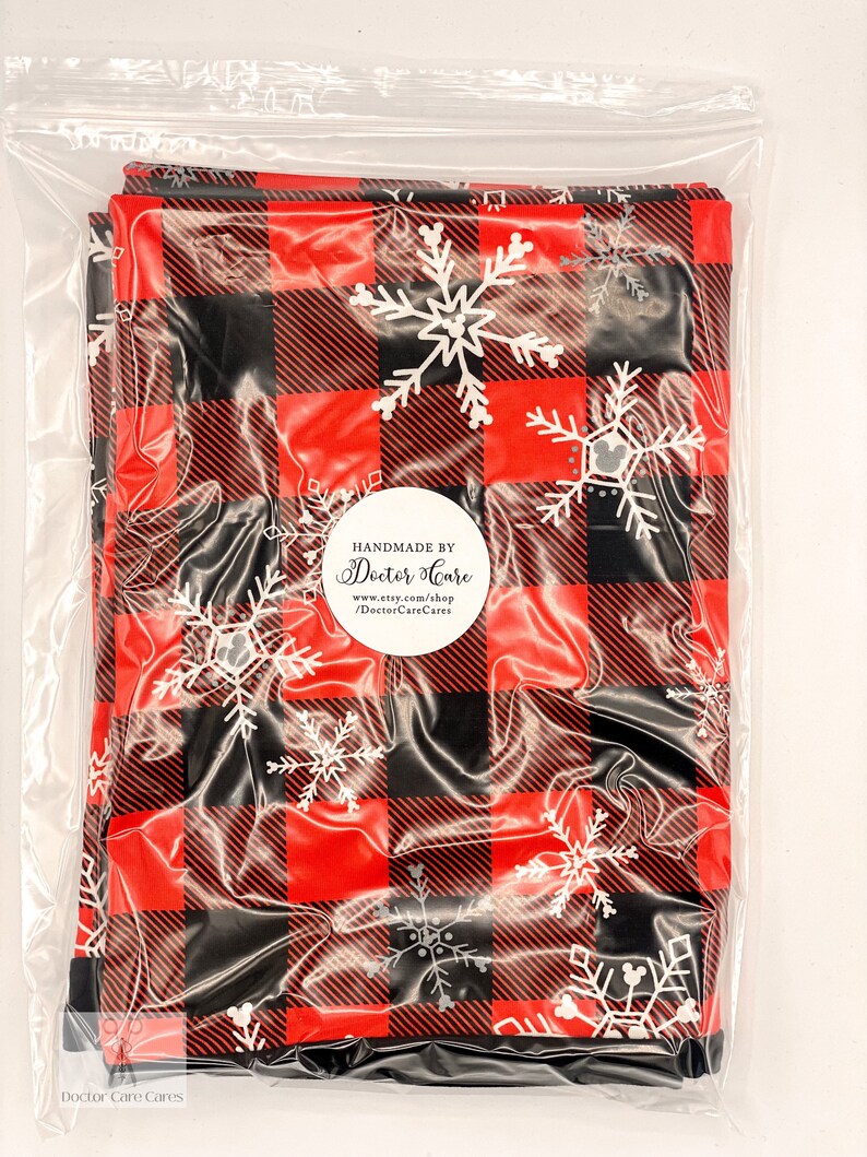 May include: A red and black buffalo plaid fabric with white snowflake designs. The fabric is packaged in a clear plastic bag with a white circle label that reads "Handmade by Doctor Care" and includes a website address.