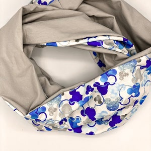 Puede incluir: Una bufanda infinita reversible con un lado gris y un lado blanco con un estampado de Mickey Mouse azul y plateado.