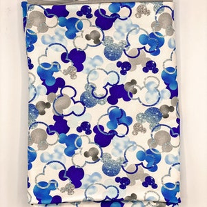 Puede incluir: Tela blanca con un patr&oacute;n de cabezas de Mickey Mouse azul y plateado con purpurina.