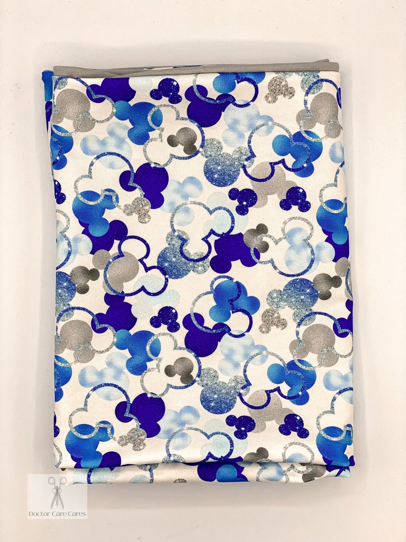 Puede incluir: Tela blanca con un patr&oacute;n de cabezas de Mickey Mouse azul y plateado con purpurina.