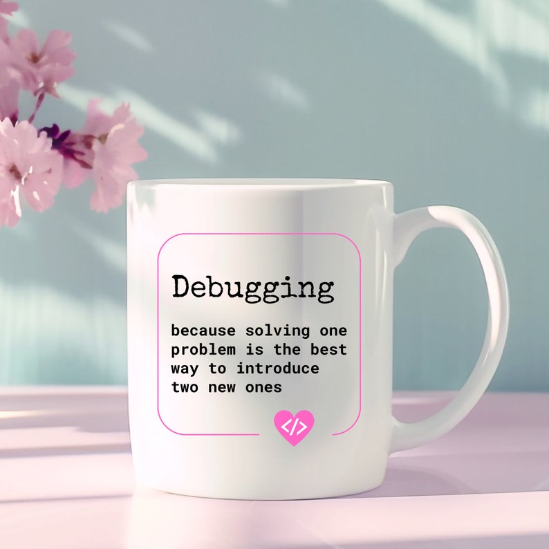 Puede incluir: Taza de cer&aacute;mica blanca con un dise&ntilde;o en negro y rosa. La taza presenta el texto "Debugging because solving one problem is the best way to introduce two new ones" y un coraz&oacute;n rosa con s&iacute;mbolos de c&oacute;digo en su interior.