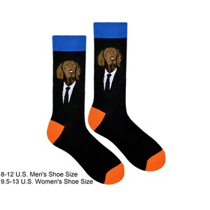 Peut inclure: Une paire de chaussettes noires avec une bordure orange et un revers bleu. Les chaussettes présentent un chien brun portant un costume et une cravate.