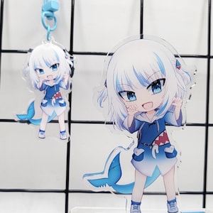 May include: A blue and white anime character keychain with a shark fin and a blue and white shark tail. The character is a girl with long white hair and blue eyes. The keychain is on a clear acrylic stand.