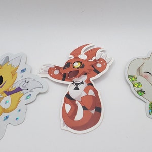 Peut inclure: Trois autocollants de personnages de dessins animés avec une finition holographique. Les autocollants représentent un personnage de renard jaune, un personnage de dragon rouge et un personnage de chien blanc.