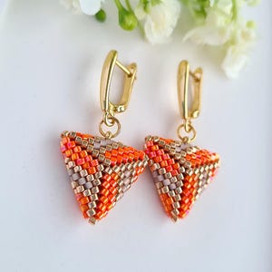 Può includere: Un paio di orecchini color oro con un design triangolare. Gli orecchini sono realizzati con piccole perline colorate nelle tonalità dell'arancione, del rosa e del grigio. Gli orecchini sono appesi a chiusure color oro.