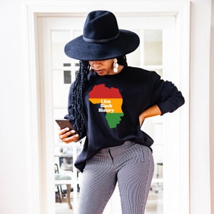 May include: A black sweatshirt featuring a graphic of the African continent in red, yellow and green colours. The graphic includes the text "I Am Black History".