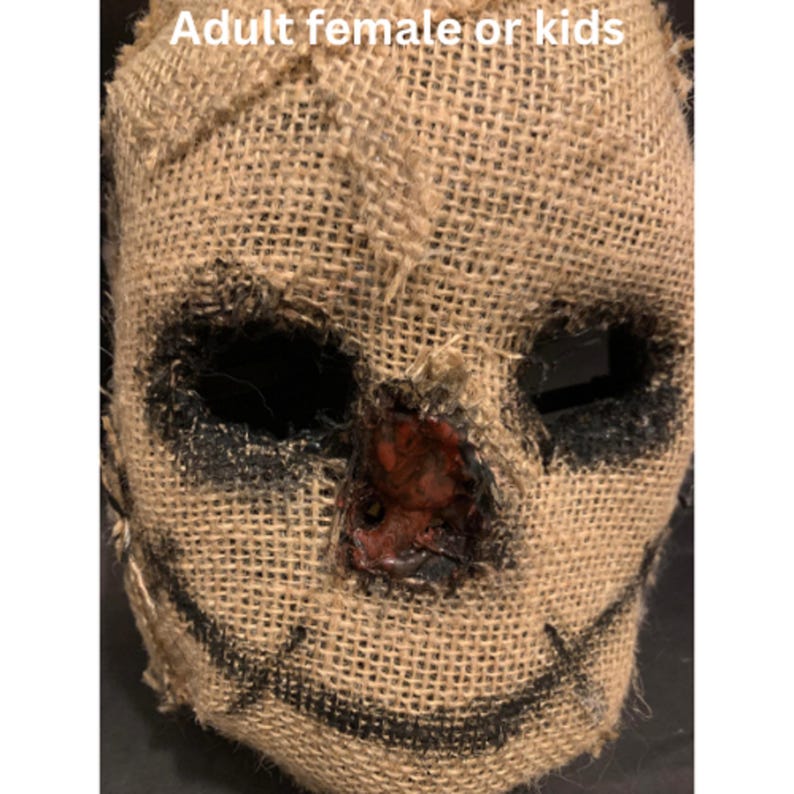 Puede incluir: Una m&aacute;scara de arpillera con agujeros negros para los ojos y una sonrisa cosida. El &aacute;rea de la nariz tiene un dise&ntilde;o rojo texturizado. El texto "Adult female or kids" est&aacute; en la parte superior de la imagen. Esta m&aacute;scara es adecuada para Halloween o eventos de disfraces.