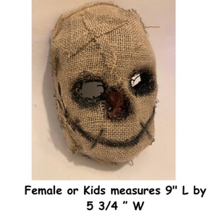 Puede incluir: Una m&aacute;scara de arpillera con costuras, detalles negros para los ojos y la boca, y una nariz marr&oacute;n rojiza. La m&aacute;scara mide 22,86 cm de largo por 14,61 cm de ancho. El texto en la imagen dice: Female or Kids measures 9" L by 5 3/4 " W.