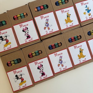 Può includere: Una collezione di scatole di cartone marrone, ognuna contenente un set di pastelli colorati. Ogni scatola presenta un'etichetta con un'illustrazione di un personaggio Disney, il nome "Marco" e il testo "2 ANNI". I personaggi includono Topolino, Minnie, Paperino, Paperina e Pluto.