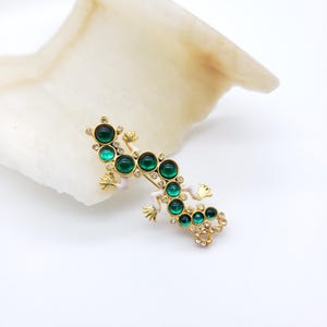 May include: A gold-tone lizard brooch with green cabochon stones and clear rhinestones.