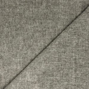 Puede incluir: Primer plano de una tela gris claro con un borde deshilachado. La tela est&aacute; doblada diagonalmente, revelando un tejido texturizado. El material parece suave y ligero, adecuado para bufandas o chales.
