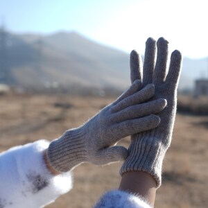 May include: A pair of gray knitted gloves with a ribbed texture. The gloves are shown with the fingers extended and the palms facing each other.