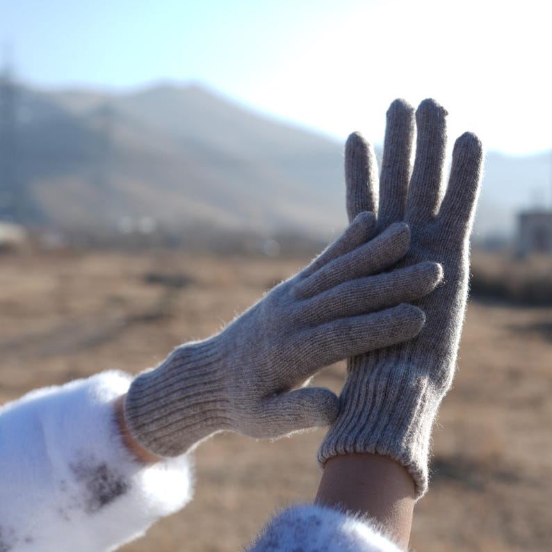 May include: A pair of gray knitted gloves with a ribbed texture. The gloves are shown with the fingers extended and the palms facing each other.