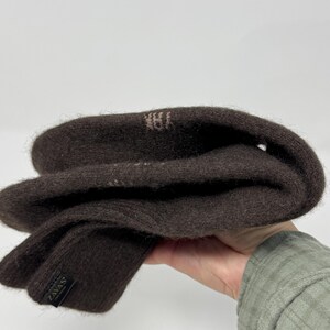 May include: A pair of dark brown knit gloves. The gloves are folded, showing the interior and exterior. The label reads "ZAVAS". The gloves are made of a soft, textured material.