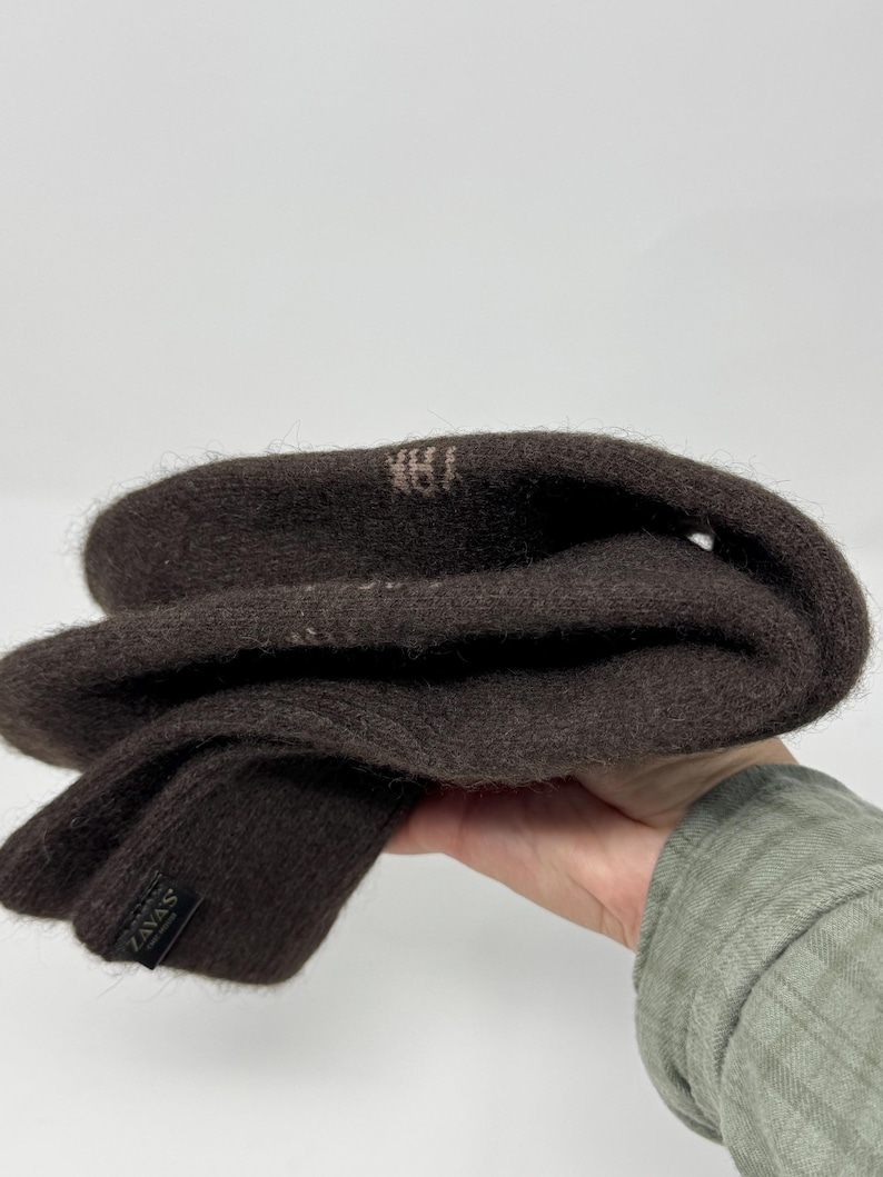 May include: A pair of dark brown knit gloves. The gloves are folded, showing the interior and exterior. The label reads "ZAVAS". The gloves are made of a soft, textured material.