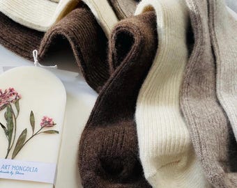May include: Four pairs of soft, knitted socks in brown, beige, and white. The socks are folded and arranged on a white surface.