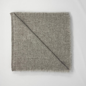 Puede incluir: Una manta gris claro doblada con un borde con flecos. La manta est&aacute; doblada diagonalmente, creando una forma triangular. La tela parece suave y texturizada, adecuada para la decoraci&oacute;n del hogar.