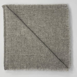 Puede incluir: Una manta cuadrada plegada, de color gris claro, con un borde con flecos. La manta est&aacute; doblada diagonalmente, creando una forma triangular. La tela parece suave y texturizada, adecuada para la decoraci&oacute;n del hogar.
