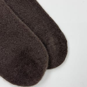 May include: A pair of dark brown socks made of a soft, fuzzy material. The socks are shown on a white background. The socks are a solid color and appear to be warm and comfortable.