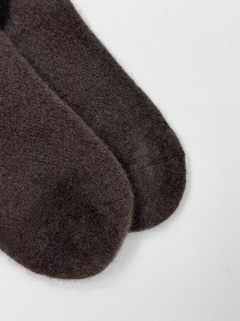May include: A pair of dark brown socks made of a soft, fuzzy material. The socks are shown on a white background. The socks are a solid color and appear to be warm and comfortable.