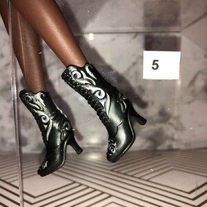 May include: A pair of black heeled boots with silver floral designs. The boots have a pointed toe and a high heel.