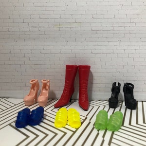 Puede incluir: Un conjunto de diez zapatos de mu&ntilde;eca en varios colores y estilos, que incluyen botas rojas, tacones rosas, sandalias negras, sandalias azules y sandalias amarillas.