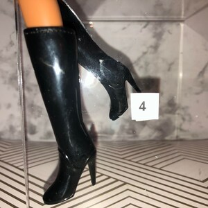 May include: A pair of black knee-high boots with high heels. The boots are made of a shiny material and have a pointed toe.