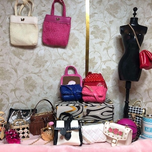 May include: A collection of miniature handbags in various styles and colors, including pink, white, blue, and black. Some bags are hanging, while others are displayed on a pink surface. A mannequin displays a red purse.