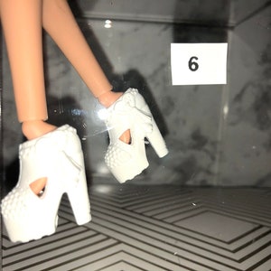 May include: A pair of white platform shoes with cutouts and bows. The shoes have a chunky heel and are made of a smooth, white material.