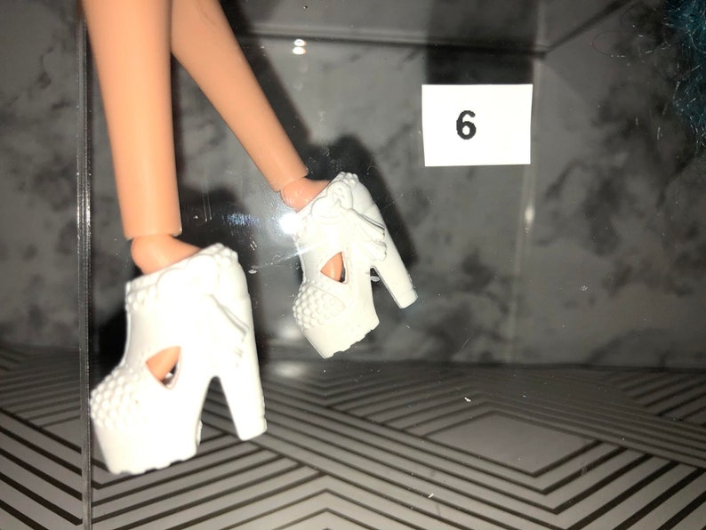 May include: A pair of white platform shoes with cutouts and bows. The shoes have a chunky heel and are made of a smooth, white material.