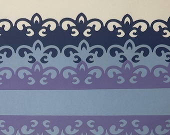 May include: A layered paper craft in shades of blue and purple. The top and bottom edges feature a decorative, cut-out design. A solid light blue band is centered, with a darker blue and purple design above and below.