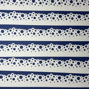 May include: Six white paper strips with a scalloped edge and a pattern of varying sized circular cutouts. The strips are arranged horizontally against a dark blue background.