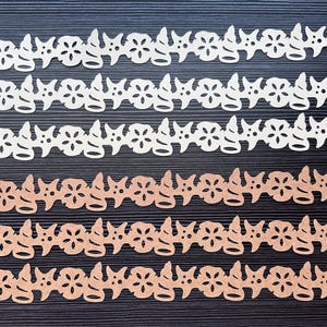 May include: Rows of decorative paper cutouts in off-white and light brown. Each cutout features a repeating pattern of flowers, starfish, and seashell shapes. The cutouts are arranged in horizontal lines against a dark background, creating a visually appealing design.
