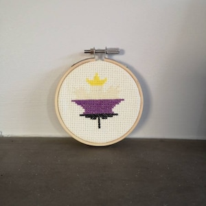 May include: A white, purple and yellow embroidered design of a maple leaf with a crown on top, in a wooden embroidery hoop.