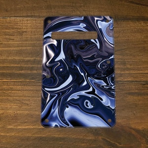 May include: A rectangular guitar pickguard with a handle cutout, featuring a swirling pattern of navy blue, white, and gray. The pickguard has pre-drilled holes for mounting on a guitar body. The design resembles a marble or liquid effect.