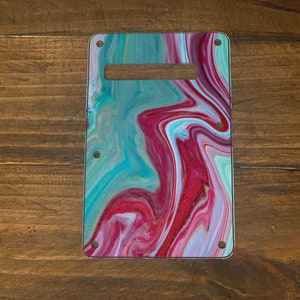 May include: A guitar pickguard with a swirling abstract design in shades of pink, teal, and white.