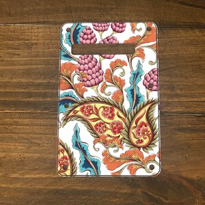 May include: A white guitar pickguard with a colorful paisley pattern. The pattern features blue, orange, yellow, and pink floral designs.