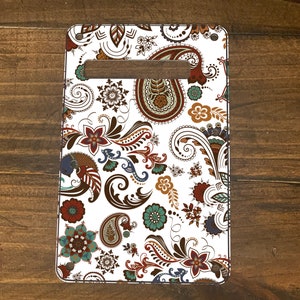 May include: Rectangular white cutting board with a handle, featuring a colorful paisley pattern in shades of brown, red, teal, and blue. The floral design is set against a white background.