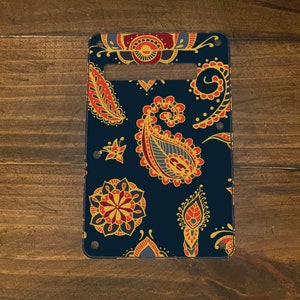 May include: A guitar pickguard with a paisley pattern in shades of red, yellow, and blue on a dark blue background.