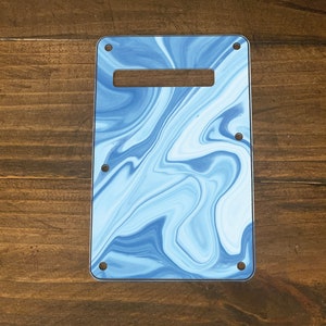 May include: Blue and white marbled guitar pickguard with a rectangular cutout for a pickup. The pickguard has a smooth, glossy finish.