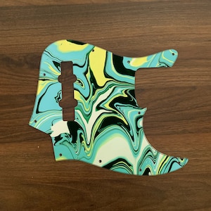 Może przedstawiać: Turkusowy, zielony, żółty i czarny marmurowy pickguard do gitary. Pickguard ma kształt gitary basowej i ma wycięcie na przetwornik.