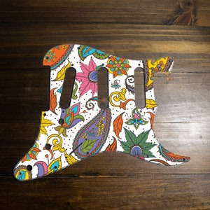 May include: A white guitar pickguard with a colorful paisley pattern. The pickguard has a floral design with orange, yellow, green, blue, and purple colors.
