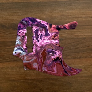 May include: A guitar pickguard with a swirl pattern in shades of purple, pink and white. The pickguard is made from clear plastic and has a glossy finish.