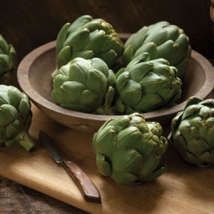 Può includere: Una ciotola piena di carciofi verdi, con carciofi aggiuntivi su un tagliere di legno accanto alla ciotola.