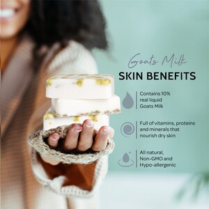 May include: Three bars of white goat milk soap with green flecks, held in a hand wearing a knitted mitten. The soap is labeled "Goats Milk Skin Benefits" and lists the benefits: "Contains 10% real liquid Goats Milk", "Full of vitamins, proteins and minerals that nourish dry skin", and "All natural, Non-GMO and Hypo-allergenic".